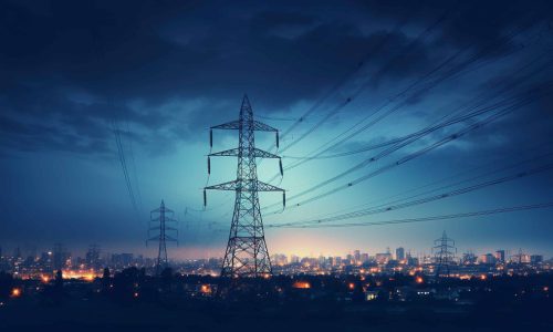 High-voltage power lines and transmission towers stretch across an urban skyline at dusk, with city buildings illuminated by lights under a moody, cloudy sky. Clarisight.com
